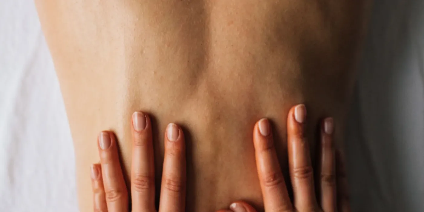 Detail dlaní masérky pracujících se spoušťovými body v oblasti zad